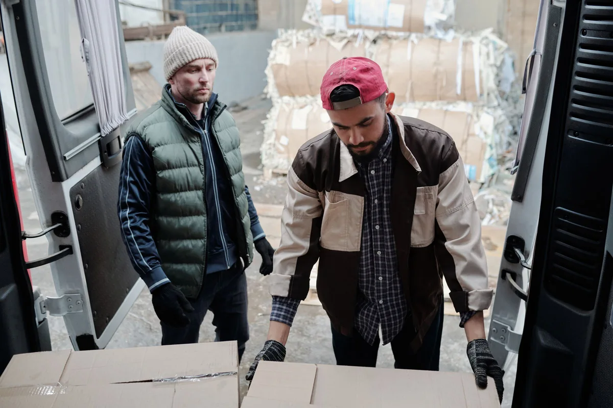 Two workers transferring cardboard boxes at the open back of a delivery van.